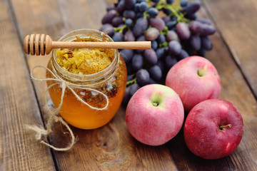 honey in a beautiful jar, wooden spoon spindle, grapes and apples on a wooden background