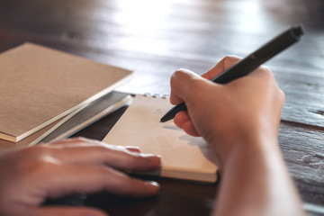 Closeup image of a woman writing on blank notebook on table in cafe