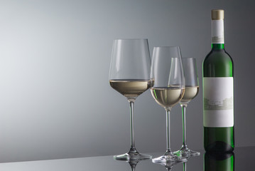 bottle of white wine with wineglass on grey background with illumination