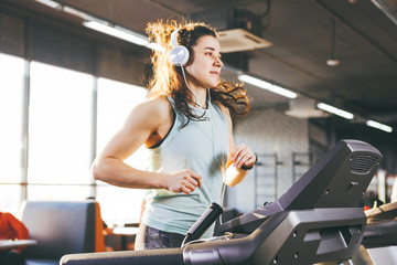 Theme is sport and music. A beautiful inflated woman runs in the gym on a treadmill. On her head are big white headphones, the girl listens to music during a cardio workout for weight loss