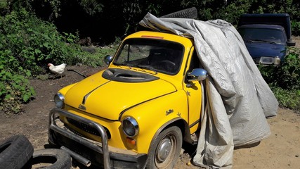 Yellow tiny retro car stands in the yard. Abandoned old vehicle