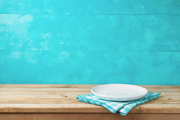 Empty white plate on wooden table with tablecloth over blue background