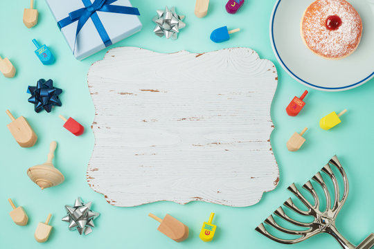 Jewish holiday Hanukkah background with wooden board, menorah, sufganiyot, gift box and spinning top.