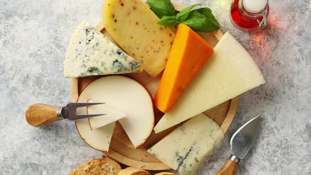 Various types of cheese served on rustic wooden board. Placed on concrete background.