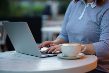 Woman using laptop by coffee cup on table at cafe