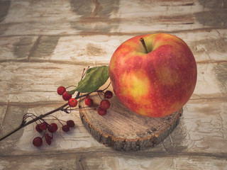 Large red apple and a twig of wild small apples on a wooden saw