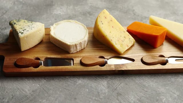 Assortment of various kinds of cheeses served on wooden board with fork and knives. Placed on concrete background.