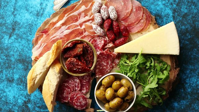 Delicious mix of different snacks and appetizers. Spanish tapas or italian antipasti on a wooden plate. View from above. Placed on blue table.