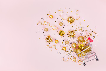 Christmas shopping cart with gift, holiday decorations and golden confetti on pink pastel...