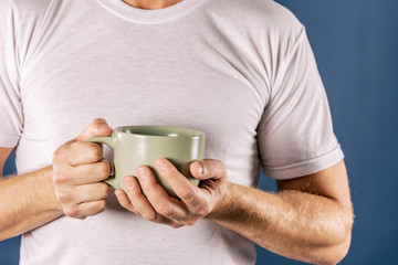 Sleepy man in white t-shirt with a mug of coffee on blue background. Early morning