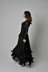 Fototapeta premium full length portrait of brunette girl wearing long black gown with corset. standing pose on grey studio background.