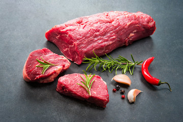 Whole piece of tenderloin with steaks and spices ready to cook on dark background