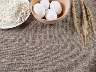 Flour, eggs in a basket and wheat ears. Baking background.