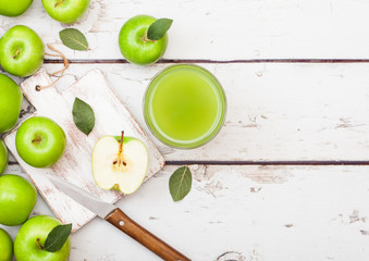 Glass of fresh organic apple juice with green apples in box on wooden background with knife