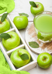 Glass of fresh organic apple juice with green apples in box on wooden background
