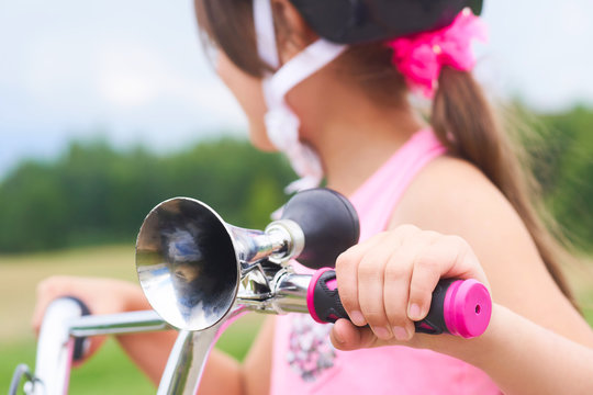 Old fashioned horn with chrome trumpet and black rubber bulb close-up mounted on a children's bike. Little girl in a pink protective helmet and pink t-shirt in the background.