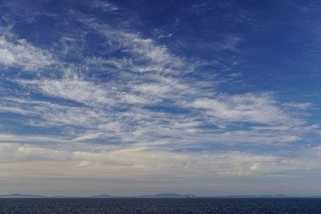 View from a cruise ship of feathery clouds over the North Pacific Ocean, mountains of the Pacific Northwest and ships in the distance.