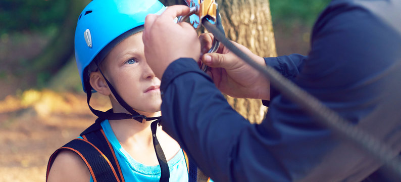 Cute little boy in blue shirt and helmet having fun at the adventure park, holding ropes and prepering to climb wooden stairs. Hobby, active lifestyle concept.
