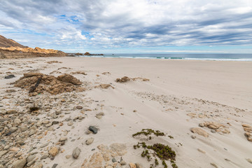 An idyllic beach at a remote location inside an arid landscape at Atacama Desert coast. The waves coming from the Pacific Ocean crash the rocks of the desert on an amazing wild dry scenery

