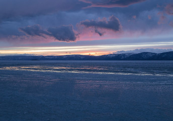 The frozen Lake Baikal. Winter landscape with tranparent ice and snow near the rocks of Olkhon Island in the sunset