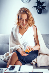 Obraz premium Vertical shot of a young student pouring some pills from the orange bottle onto her palm. Sick girl in blacket pours some drugs.