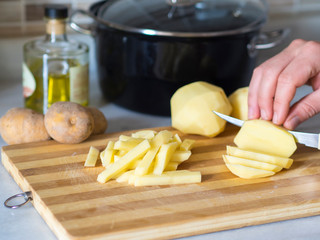 ingredients for french fries. person chopping potatoes on the board with knife
