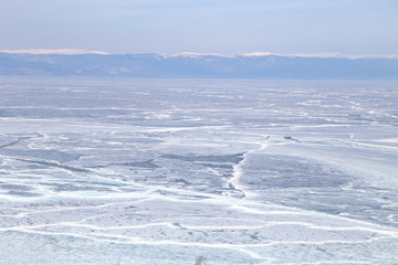Cracks on the surface of the blue ice. Frozen lake in winter mountains. It is snowing. Lake Baikal. Winter