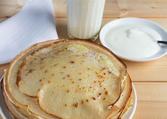 Fried pancakes with butter, a glass of milk, sour cream on a wooden table.