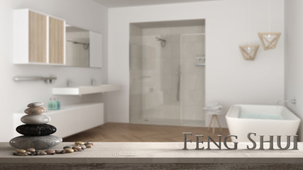 Wooden vintage table shelf with pebble balance and 3d letters making the word feng shui over blurred bright bathroom with double sink, shower and bathtub, zen concept interior design