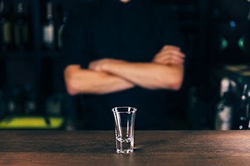 Obraz na płótnie Canvas Barmen hand with bottle pouring beverage into glass. Bartender pouring strong alcoholic drink into small glass on bar, shots, on bright background.