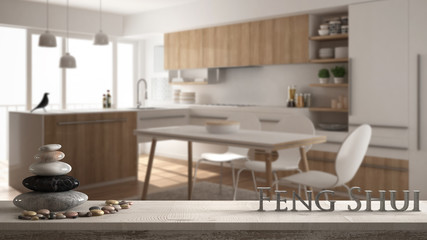 Wooden vintage table shelf with pebble balance and 3d letters making the word feng shui over blurred minimalistic wooden kitchen with dining table and carpet, zen concept interior design