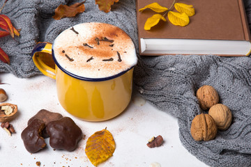 Kubek kawy z goździkami i cynamonem otoczony jesiennymi liśćmi i ciepłym szalem. 