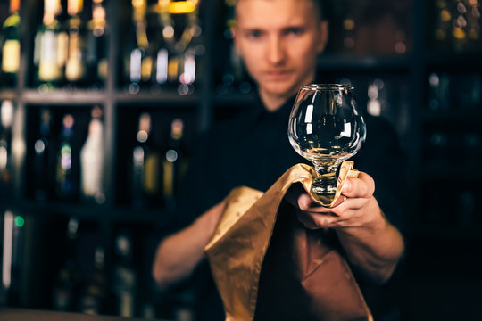 Barman is cleaning the glass with a cloth at bar counter background. The bartender cleaning the glass on the bar - Powered by Adobe