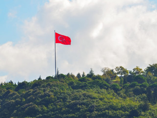 Turkish flag on a green wooded hill on a background of clouds and blue sky clouse up.
