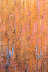 Peeling pink and orange paint on decaying wood panel fence/door