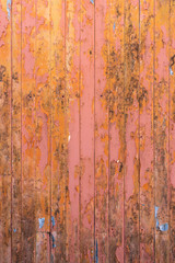 Peeling pink and orange paint on decaying wood panel fence/door