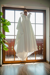 Bride's white wedding dress hanging in front of the window