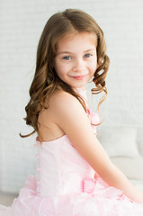 Portrait of a little girl in a white dress sitting in a bright room on the bed