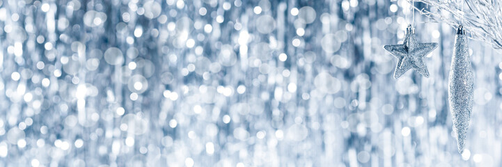 Shiny silver christmas ornaments hanging on a tree, with defocused christmas lights in the...
