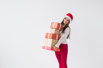 Christmas and holidays concept - young woman in santa hat holding stack of gift boxes over white background with copy space