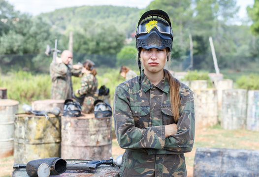 Female paintball player in camouflage and black mask with traces of paint