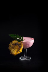 Cold pink cocktail in a glass with ice and a piece of pineapple on the grill. Restaurant serving on a black background.