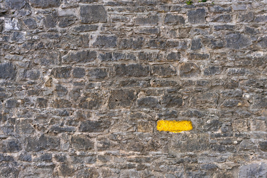 Old gray stone wall with one stone highlighted painted bright yellow
