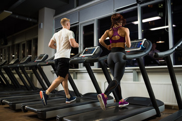 Fototapeta na wymiar Sporty and slender couple running on the treadmills.