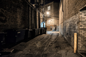 Fototapeta na wymiar Dark and scary downtown urban city street corner alley with an eerie vintage industrial warehouse factory entrance and dirty dumpsters at night