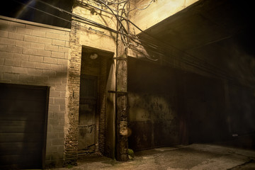 Dark and scary downtown urban city street corner alley with an eerie vintage industrial warehouse factory entrance door and a loading dock at night - Powered by Adobe
