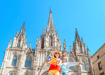Two Happy woman tourists having fun and travel with catalan flag near the Cathedral in Barcelona...