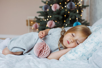 Little girl sleeps with a toy of house at Christmas tree