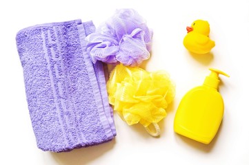 Purple terry towel, yellow and lilac sponges, liquid soap and rubber duck. Flat lay baby bath products