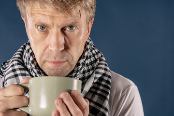 Man in a checkered scarf with big mug suffering from a sore throat and headache. Blue background